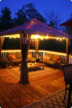 a gazebo with lights on it is lit up in the evening time and sits on a wooden deck