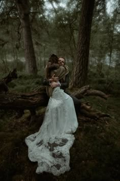 a man and woman are sitting on a tree branch in the woods, hugging each other