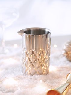 a silver pitcher sitting on top of snow covered ground next to a wine glass and spoon