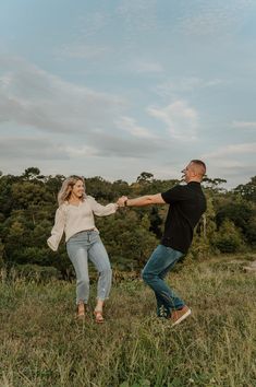 a man and woman holding hands while standing on top of a grass covered field with trees in the background