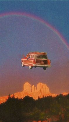 an old car is flying in the air with a rainbow above it and mountains behind