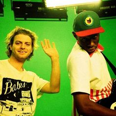 two young men standing next to each other in front of a green screen with their hands up