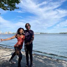 two people standing next to each other near the water