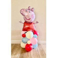 a peppa pig balloon sitting on top of a pile of balloons in front of a wall