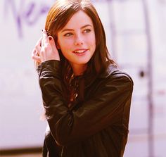 a beautiful young woman standing next to a white wall holding her hand on her head