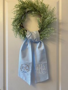 a wreath hanging on the front door with a monogrammed scarf tied around it