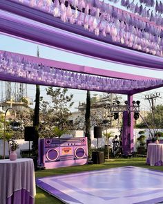 an outdoor dance floor with purple decorations and lights hanging from it's ceiling, in the middle of a lawn area