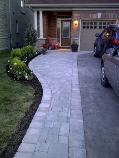 a car parked in front of a house next to a driveway with plants and flowers