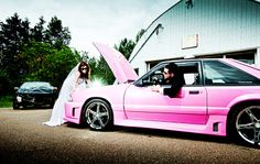 a bride and groom are sitting in the hood of a pink car