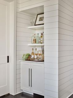 a kitchen with white walls and shelves filled with wine glasses on top of the counter