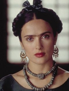 a woman wearing a necklace and earrings with a black bow on her head is looking at the camera