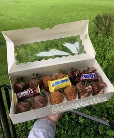 someone is holding a box full of chocolates and candy bars in front of some bushes