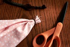 an orange pair of scissors sitting on top of a table next to a pink cloth