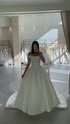 a woman in a white wedding dress taking a selfie with her cell phone while looking at the camera