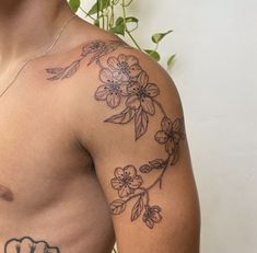 a man with a flower tattoo on his arm and chest, standing in front of a plant