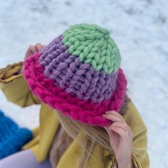 a woman wearing a knitted hat while sitting in the snow with her hand on her ear