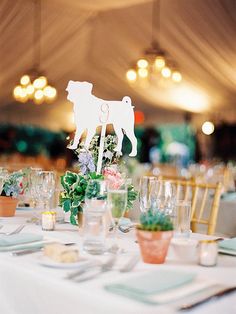 the table is set for an event with flowers and greenery in vases on it