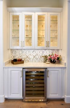 a kitchen with white cabinets and marble counter tops in the center is filled with wine glasses