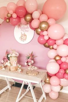 a table topped with lots of pink and gold balloons next to a white table covered in cake