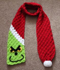 a crocheted scarf with an angry grin face on it and a red santa hat