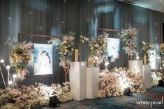 an arrangement of flowers and candles on display in front of a wall with pictures behind them