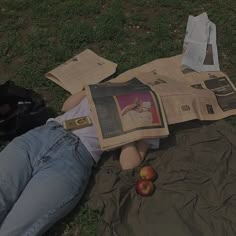 a person laying on the ground reading a newspaper with an apple in front of them