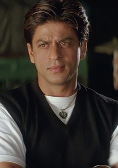 a man with his arms crossed in front of him, wearing a black vest and white t - shirt