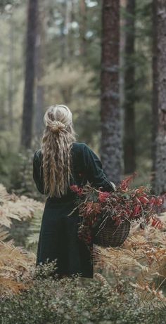 a woman with long hair walking through the woods carrying a basket full of berries in her hand