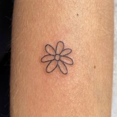 a small black flower tattoo on the right side of the arm, with an arrow in it's center