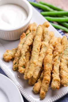 some fried food on a white plate next to green beans and dipping sauce in a bowl