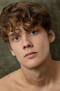 a young man with curly hair and no shirt looking at the camera while wearing an unbuttoned t - shirt