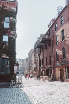 people are walking down the cobblestone street in an old city with red brick buildings