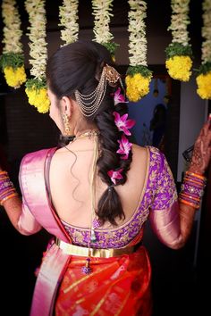 a woman in a red and pink sari with flowers on her head is holding something