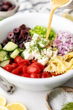 a bowl filled with pasta salad and dressing being drizzled over it