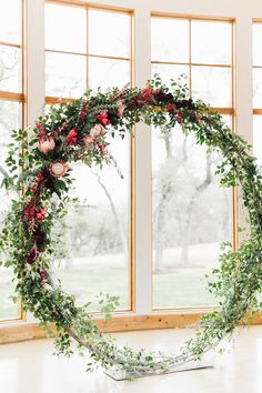 a floral wreath with greenery and red flowers in front of large windows