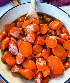 a bowl filled with cooked carrots on top of a wooden spoon next to a purple towel