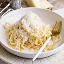 a white plate topped with pasta covered in parmesan cheese next to silverware