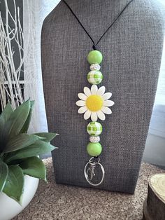 a necklace with green beads and a white flower on it next to a gray mannequin