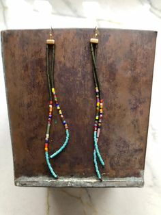 two long beaded earrings hanging from a hook on a metal stand in front of a marble wall