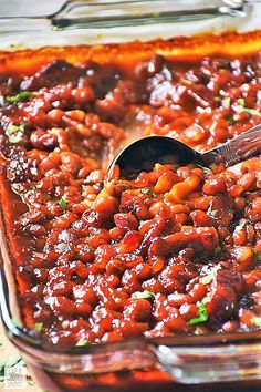 a casserole dish full of beans and meat with a spoon in the casserole