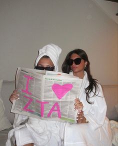 two women sitting on a couch while reading a newspaper with the word i love azz written on it