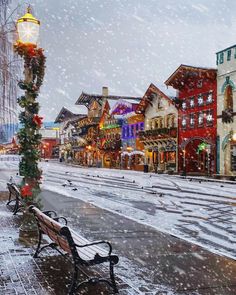 a bench sitting on the side of a road in front of buildings covered in snow