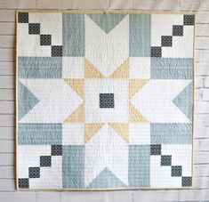 a quilted wall hanging on the side of a white brick wall with a yellow and blue star design