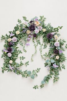 an arrangement of flowers and greenery arranged on a white wall with green leaves around it