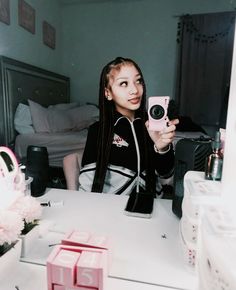 a young woman taking a selfie in her bedroom with flowers and makeup on the table