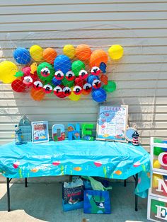 a blue table topped with lots of balloons and toys next to a wall covered in paper lanterns