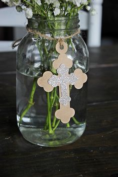 a mason jar filled with flowers and a wooden cross hanging from the front, on a table