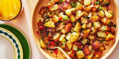 a bowl filled with cooked potatoes next to plates and orange juice on a table top