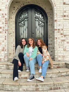 three young women sitting on steps in front of a door, one is covering her mouth