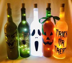 halloween wine bottles with lighted faces and pumpkins on them, all lined up in a row